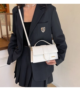 Close-up of a minimalist white leather crossbody bag with a gold metal brand logo