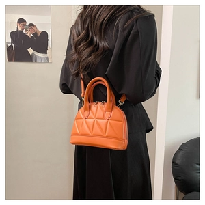 Orange shell-shaped handbag with geometric quilting shown worn with a black dress