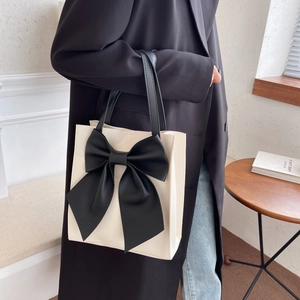 Chic cream tote bag featuring a large black bow design and contrast shoulder straps