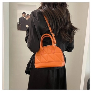 Detail view of bright orange shell bag with triangular quilted texture on black dress