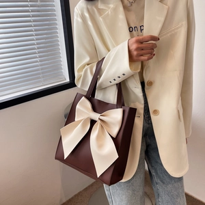 Large brown tote bag with oversized white bow accent and elegant leather handles