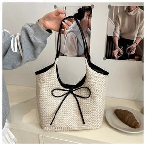 Détail du sac cabas en paille tissée avec nœud noir et fines anses en similicuir