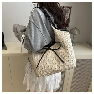 Gros plan d'un sac en paille tressée beige avec détail de nœud noir et bandoulière