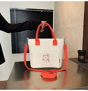 Detail of cream canvas bag with orange straps and a cute red cartoon bear illustration