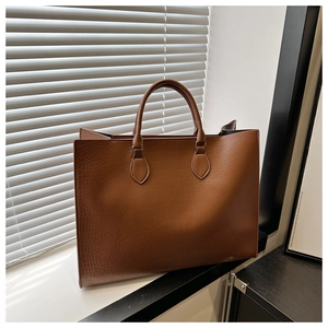 Détail d'un grand sac cabas marron à motif crocodile avec poignées arrondies sur rebord de fenêtre