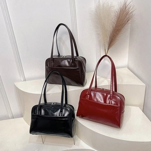 Three elegant shiny leather pillow bags in black, brown and red on a display stand