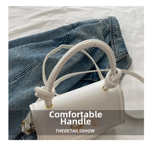 Detalle de bolso blanco con lazo metálico dorado y diseño de asa anudada de tendencia