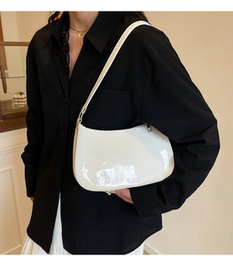 Close-up of a white glossy patent leather baguette bag worn as an underarm shoulder bag