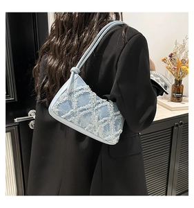 Dettaglio borsa a spalla in denim azzurro con texture floreale sfrangiata indossata dal modello