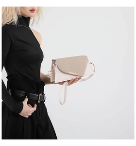 Detail van een beige crossbodytas met geweven flap en gouden gesp gedragen door model