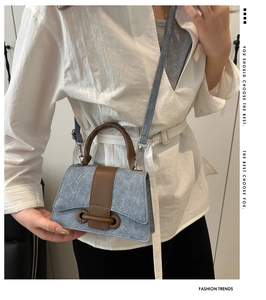 Detail of light blue denim handbag with brown leather accents on white outfit