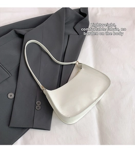 Close-up of a white crescent shoulder bag with golden buckles on a grey blazer