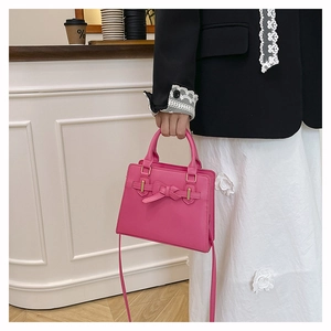 Detail of rose pink handbag with bow design and gold hardware held by a model