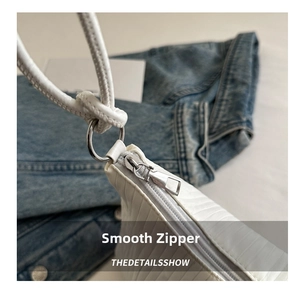 Detail of white textured handbag showing silver metal zipper and smooth finish