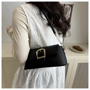 Detail of minimalist black leather crossbody bag with a prominent gold buckle and chain strap