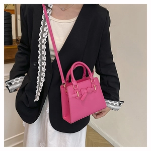 Detail of pink satchel bag with gold buckle bow on a model wearing black suit
