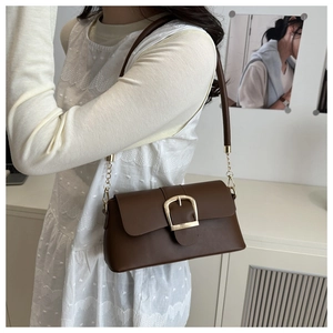 Detailed view of dark brown leather underarm bag with gold square buckle and chain strap