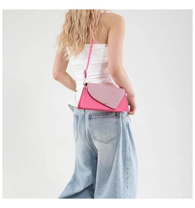 Detail van fuchsia crossbodytas met getextureerde klep op model in witte top en jeans