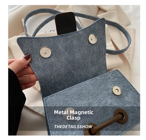 Detail view of the magnetic buckle closure on a blue-grey suede textured crossbody bag