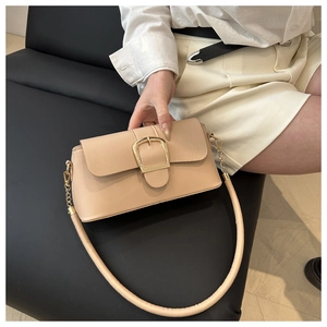 Close-up of minimalist beige leather underarm bag featuring a large gold square buckle