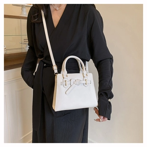 Witte crossbodytas met strik gedragen door een model in een zwarte jurk in een studio