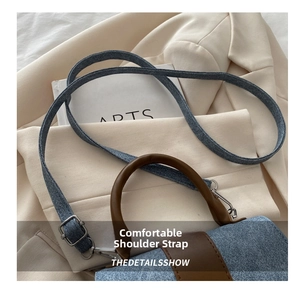 Detail view of denim crossbody bag with brown leather handles on a beige blazer