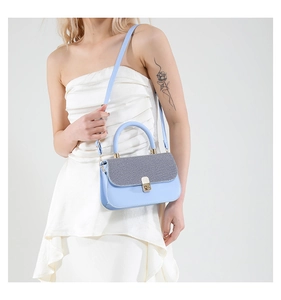Detail view of stylish blue leather bag with gray woven flap and gold metal lock buckle