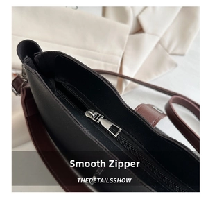 Close-up of smooth metal zipper and brown leather shoulder strap on a bucket bag