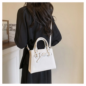 Detail van witte leren handtas met strik en gouden ring gedragen door een model
