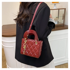 Detail of burgundy quilted patent leather mini bag with gold key charm and fine shoulder strap