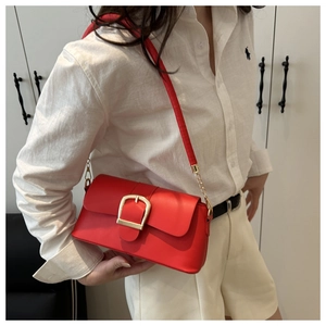 Detail view of a bright red leather crossbody bag with a large golden metal buckle
