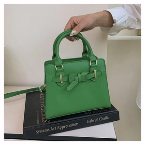 Close-up of green leather handbag with bow buckle and gold hardware on black books
