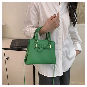 Close-up of green elegant handbag with bow knot detail on model with white shirt