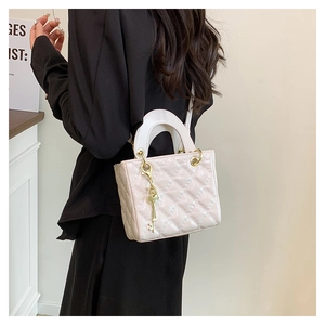 Close-up of quilted cream leather handbag with gold key pendant and metallic hardware