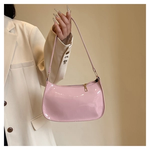 Detail of pink glossy patent leather shoulder bag with gold zipper held by a model