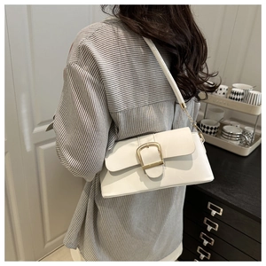 Detailed close-up of white leather shoulder bag featuring a large golden horseshoe buckle