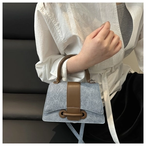 Detail of light blue textured mini handbag with dark brown leather trim and silver hardware