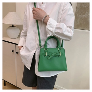 Close-up of green elegant shoulder bag with decorative leather knot and gold hardware