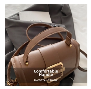 Close-up of brown leather handbag featuring a large gold metal buckle and wide handle
