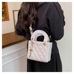 Detailed back view of model wearing white quilted handbag with golden key charm and strap