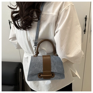 Detail of blue textured crossbody bag with brown leather handles and silver hardware