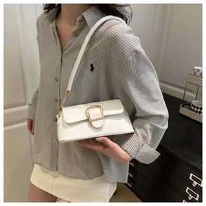Detail of white leather shoulder bag with large gold buckle and chain strap on a model
