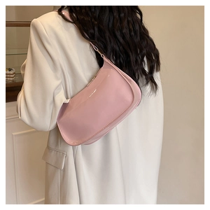 Close-up of a glossy light pink patent leather shoulder bag worn with a white blazer