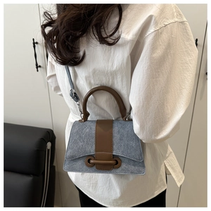 Detail of blue denim trapezoid handbag with brown leather trim and metal ring hardware