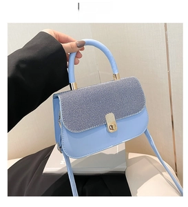Détail du sac bandoulière bleu clair avec rabat texturé et fermoir rotatif doré