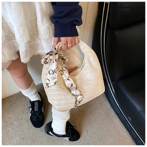 Gros plan d'un sac demi-lune en paille beige avec poignée décorée d'un foulard en soie