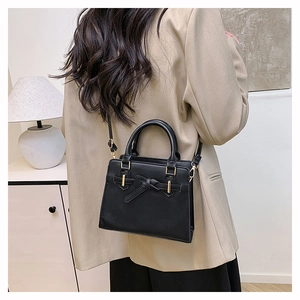 Detail view of black square handbag with bow accent and gold hardware on beige blazer