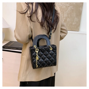 Detail of black quilted leather handbag with gold key charm shown on model