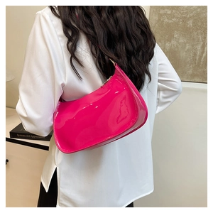 Detailed view of the glossy rose pink patent leather baguette bag worn as a shoulder bag