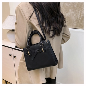 Detail of minimalist black leather handbag with belt buckle and dual handles worn by model